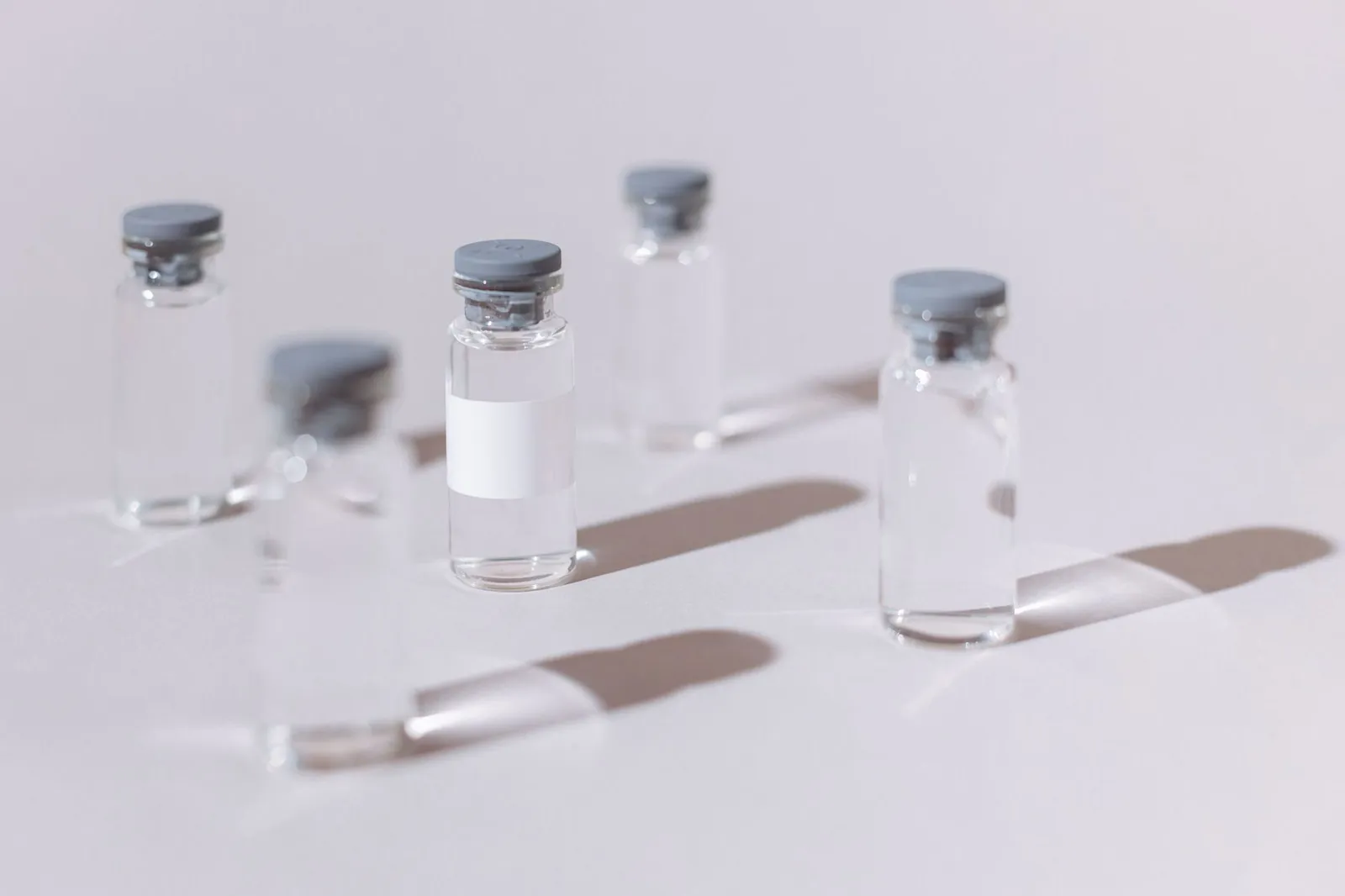 Clear glass vials used for vaccines or medication, displayed on a sterile white surface. Stock photo illustrating Gland Pharma's new order story.