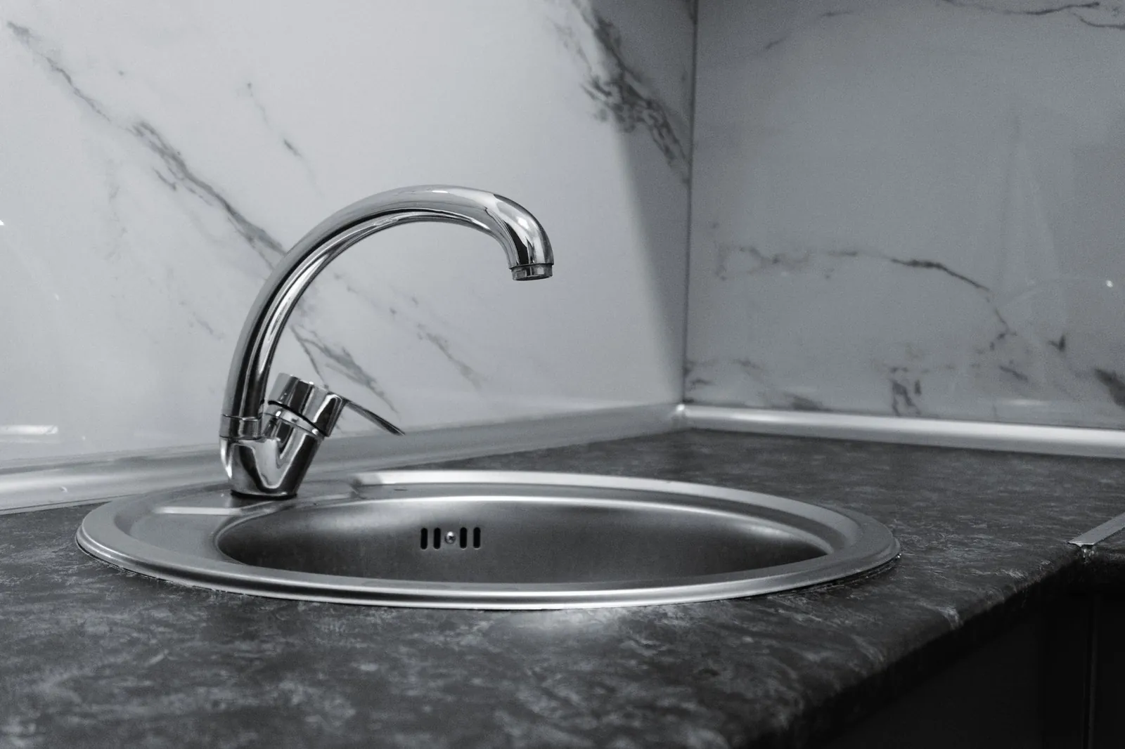 Stainless steel kitchen sink and faucet against marble backsplash in a modern kitchen. Stock photo illustrating Carysil's production started story.