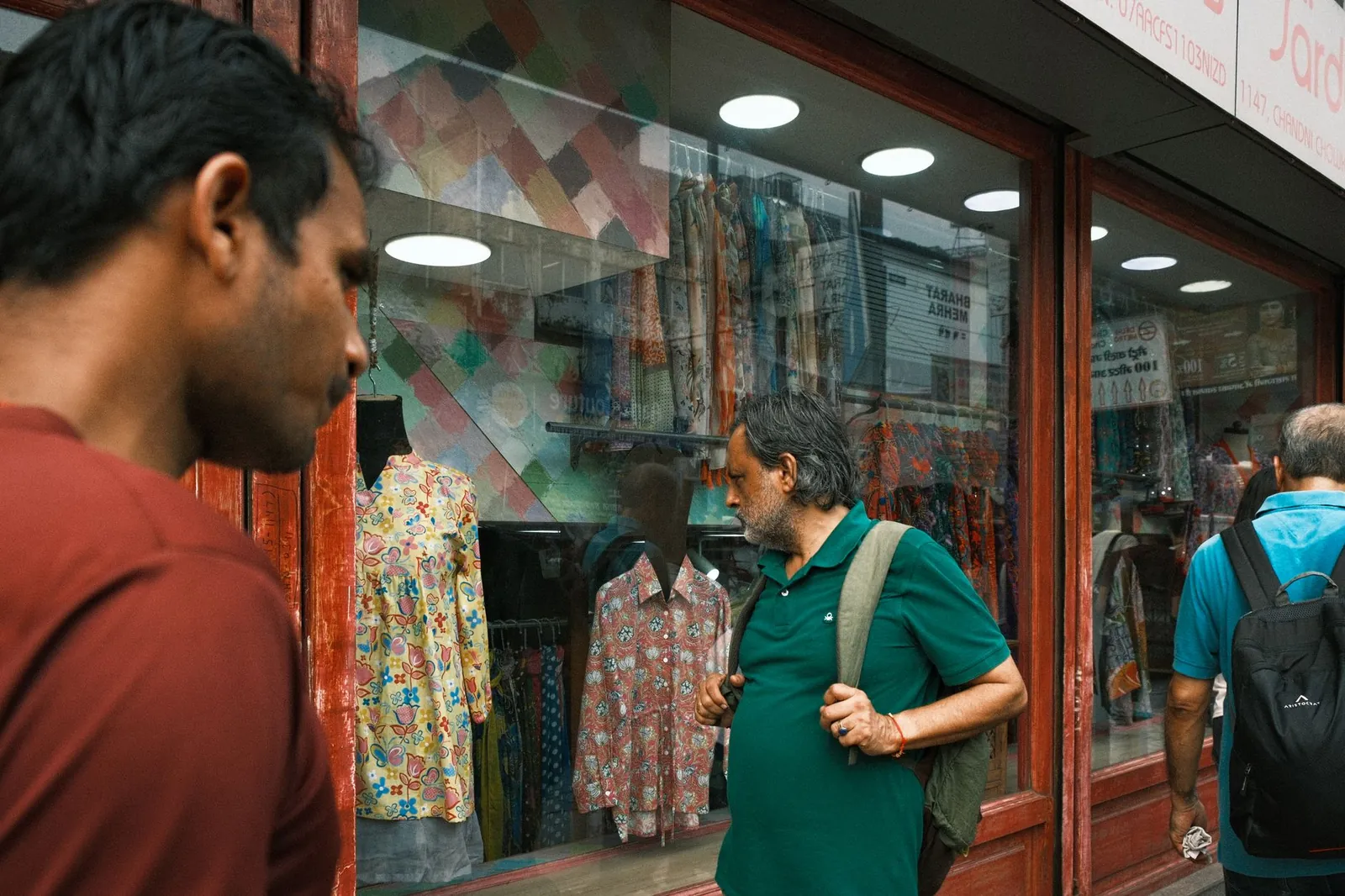 Men browsing colorful clothing at a bustling street market in Delhi, India. Stock photo illustrating Nandani Creation's expansion story.