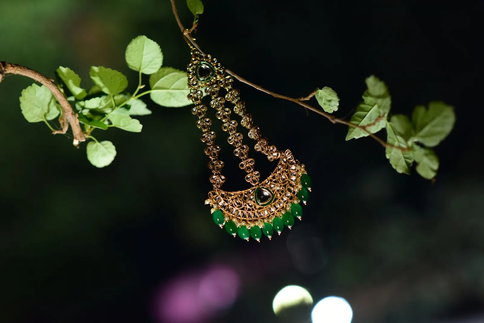 Intricate gold necklace with green gemstones hanging on a tree branch, emphasizing traditional Indian craftsmanship. Stock photo illustrating SMR Jewels' product launched story.
