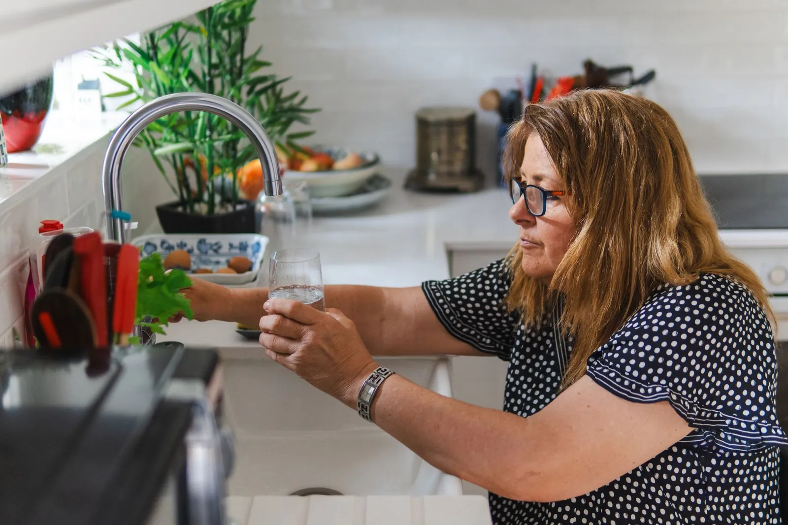 A middle-aged woman filling a glass with water in a modern kitchen setting. Stock photo illustrating Urban Company's product launched story.