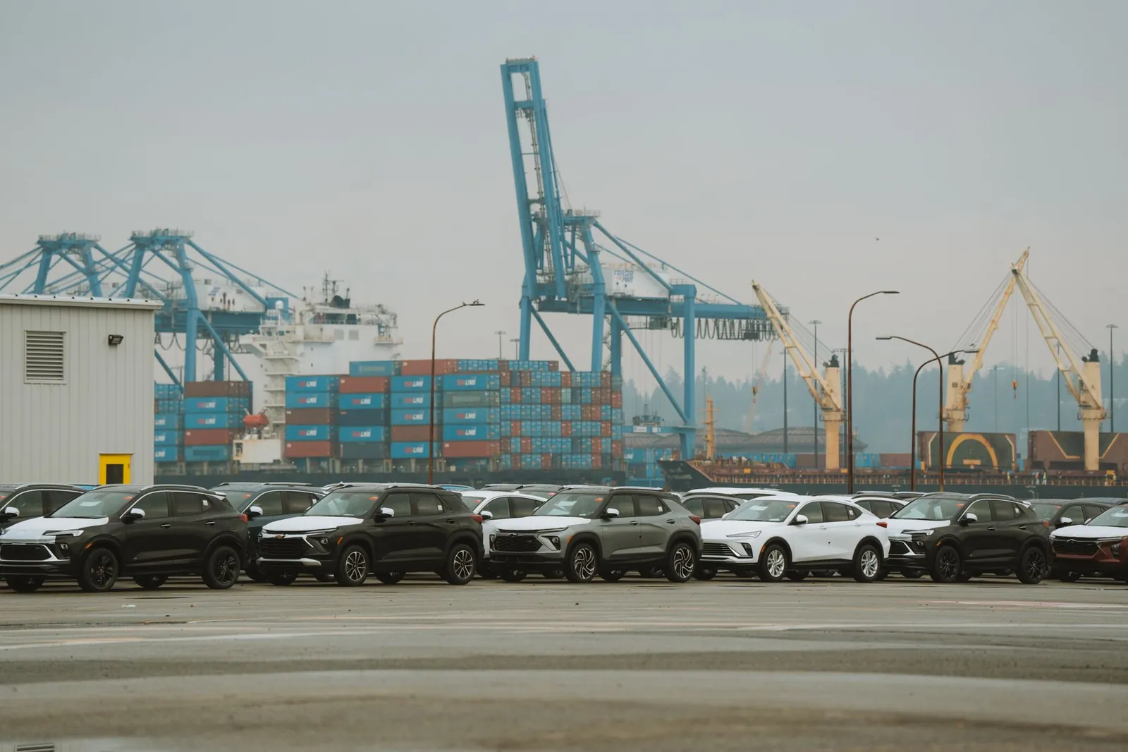 A lineup of parked cars at a bustling industrial shipping port with cranes and containers. Stock photo illustrating Hyundai Motor India's earning call story.