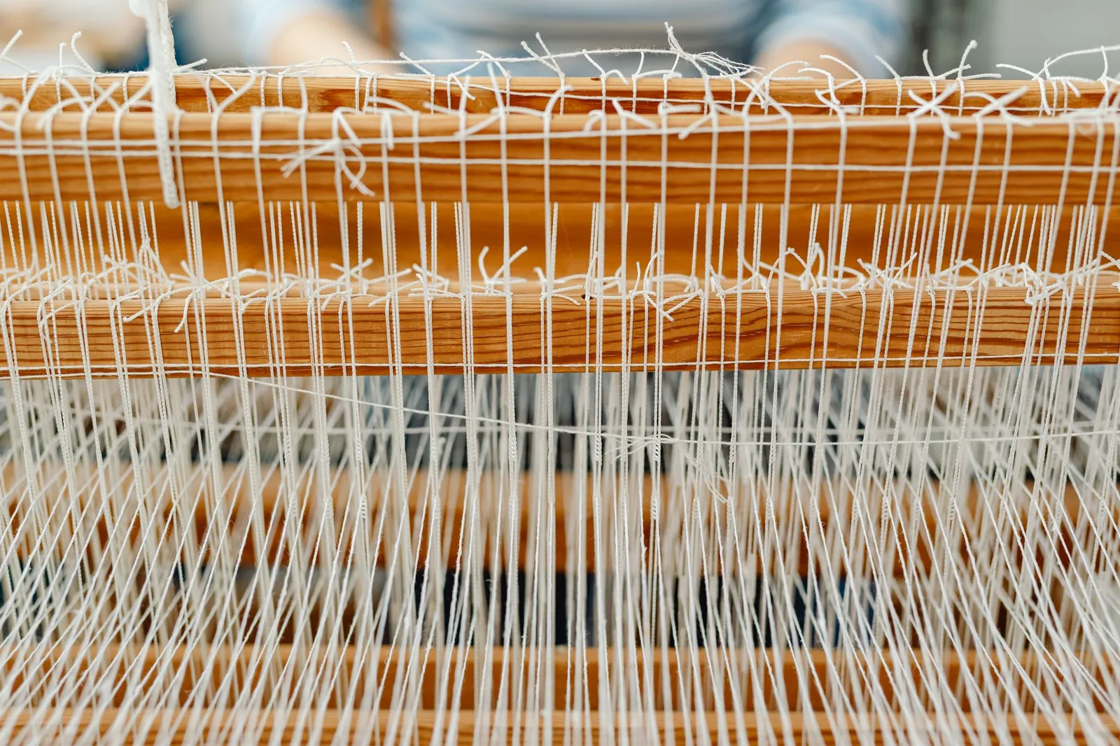 Detailed close-up of a wooden loom with white threads, showcasing traditional weaving. Stock photo illustrating Arvind's fund raise story.