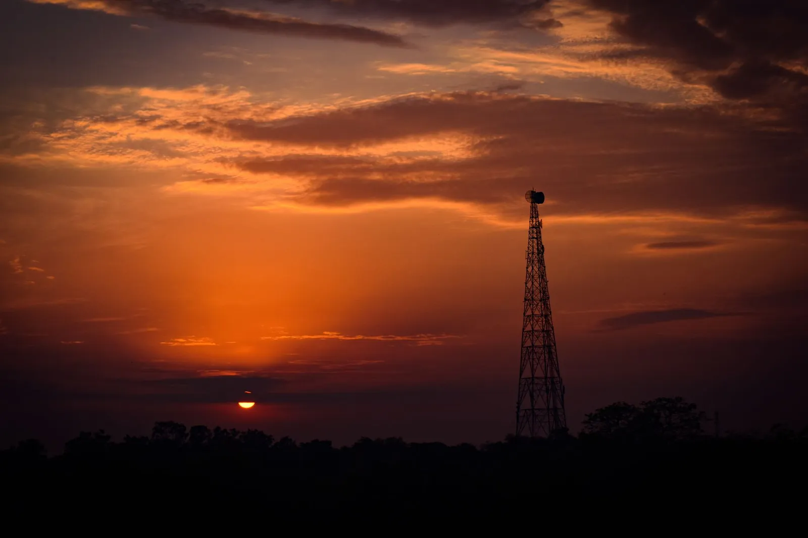 A striking sunset with a silhouetted telecom tower against vibrant skies. Stock photo illustrating Bharti Airtel's expansion story.