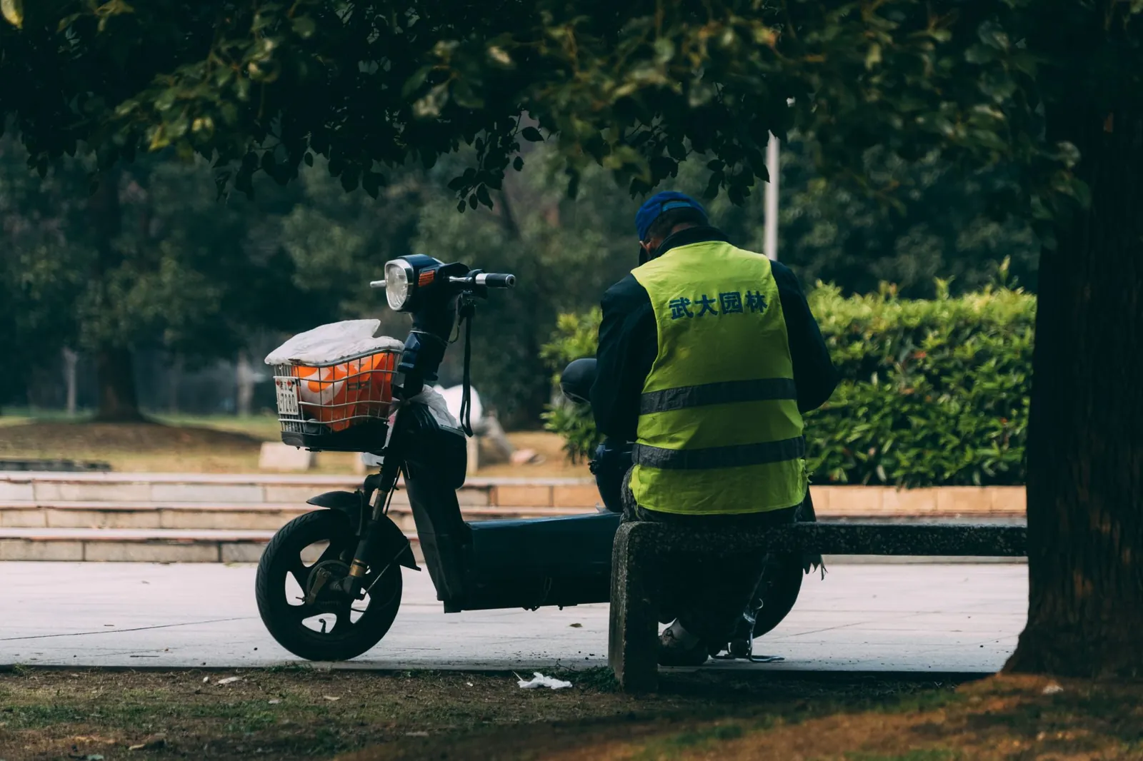 A man in a reflective vest sits on a bench next to a scooter in a city park. Stock photo illustrating Ather Energy's product launched story.