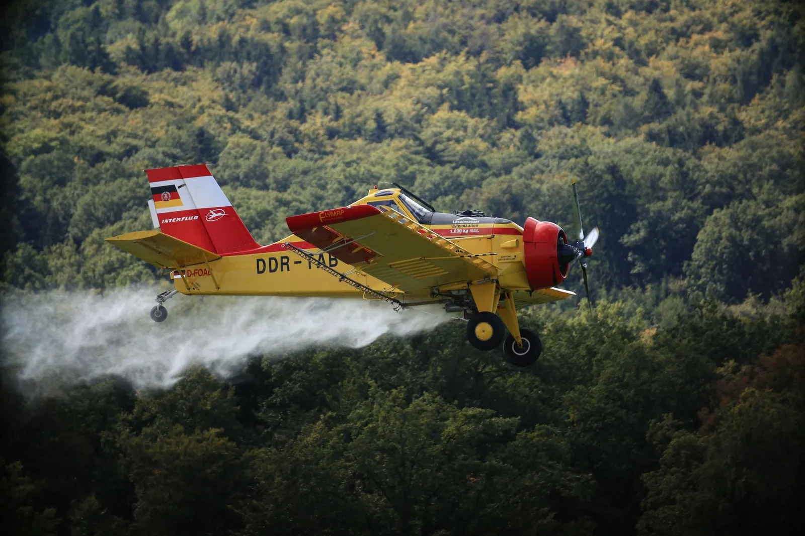 Yellow crop dusting plane spraying chemicals over lush green forests. Stock photo illustrating Gujarat State Fertilizers & Chemicals' product launched story.