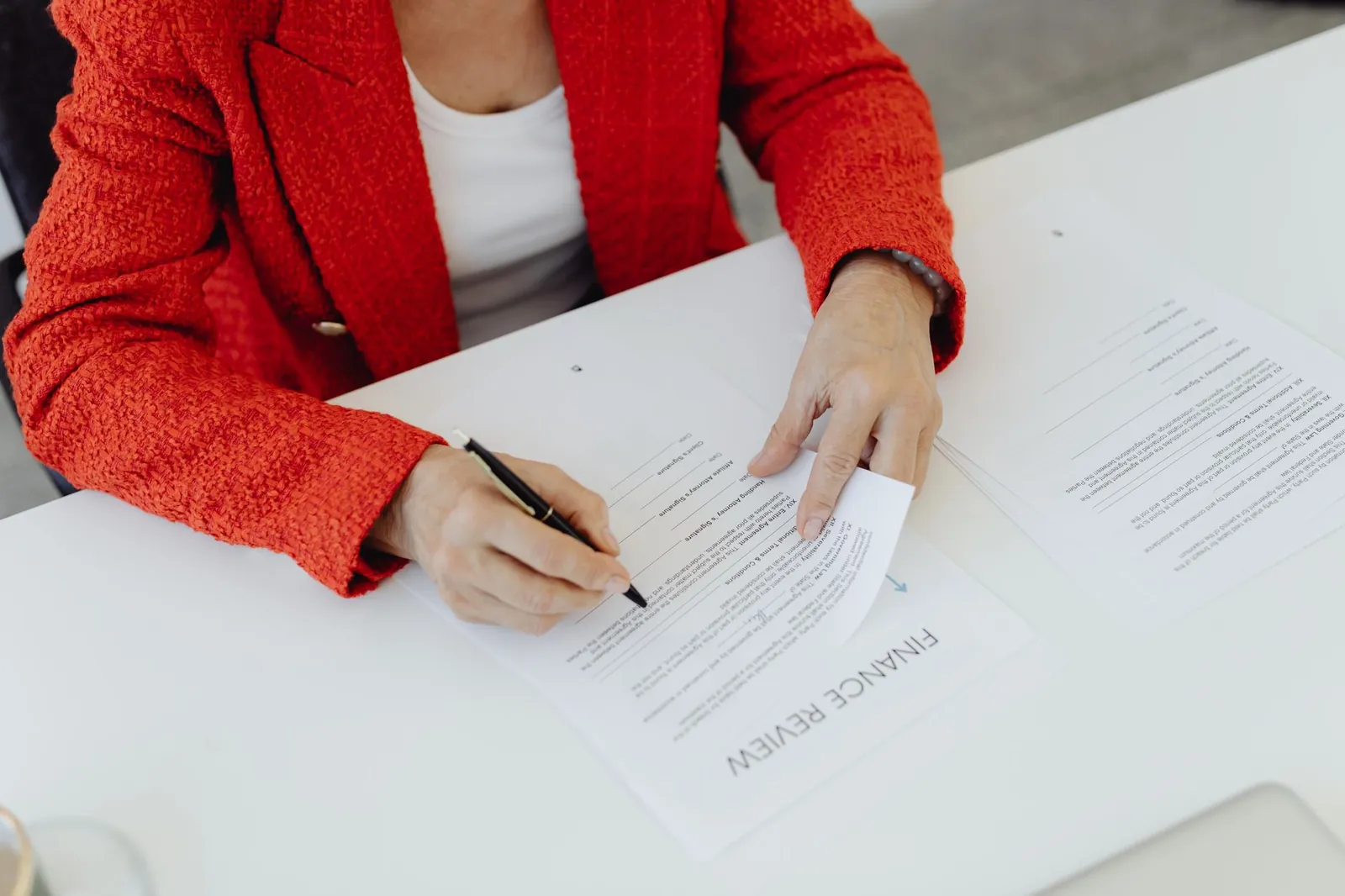 Close-up of a businesswoman in a red blazer signing finance documents at an office desk. Stock photo illustrating Share India Securities' fund raise story.
