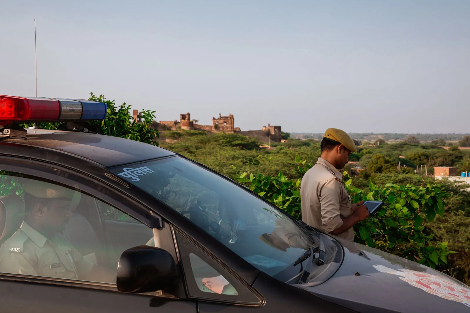 Police officer using tablet beside patrol car in scenic outdoor setting. Stock photo illustrating Blue Cloud Softech Solutions' product launched story.