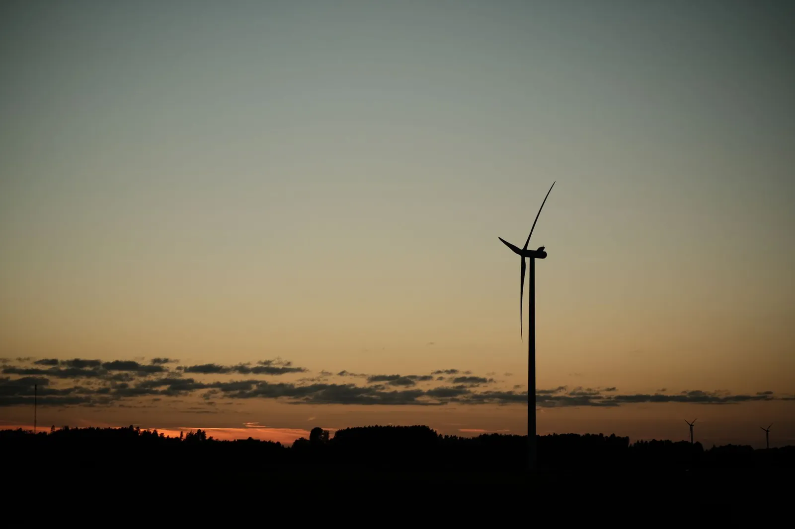A solitary wind turbine stands against a colorful sunset, symbolizing renewable energy. Stock photo illustrating Alpex Solar's earning call story.