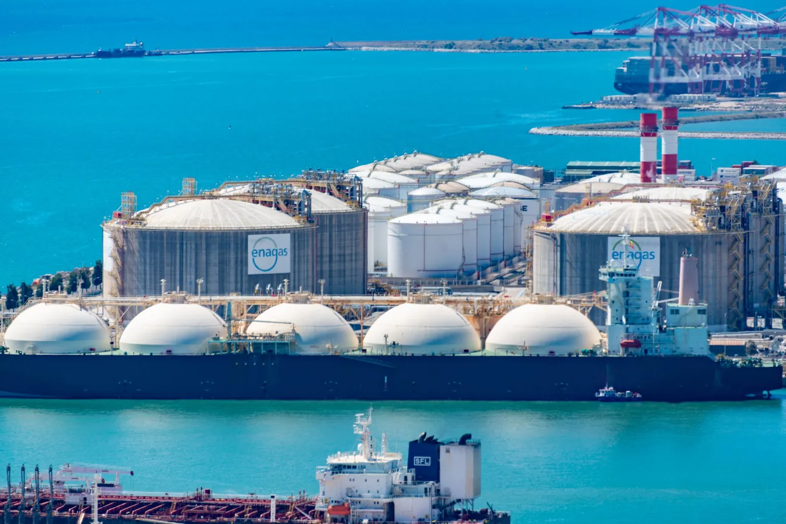 Aerial shot of a gas terminal featuring LNG storage tanks and tanker ships in turquoise waters. Stock photo illustrating Aegis Logistics' fund raise story.