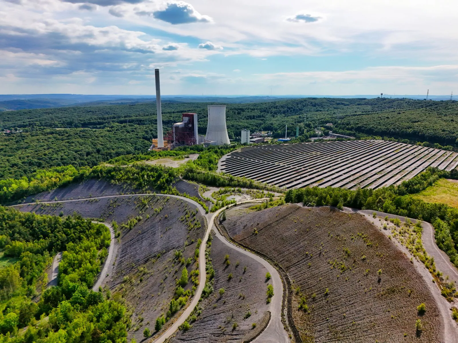 Aerial view of power plant and solar farm amidst lush greenery and hills. Stock photo illustrating Amanta Healthcare's production started story.