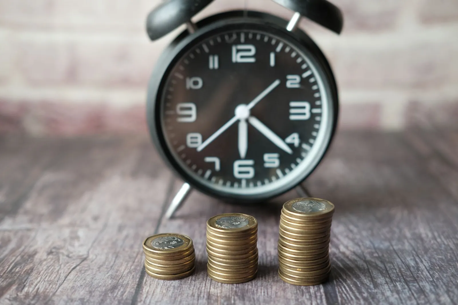 Stacked coins and a classic alarm clock symbolize the value of time and money. Stock photo illustrating Unifinz Capital India's fund raise story.