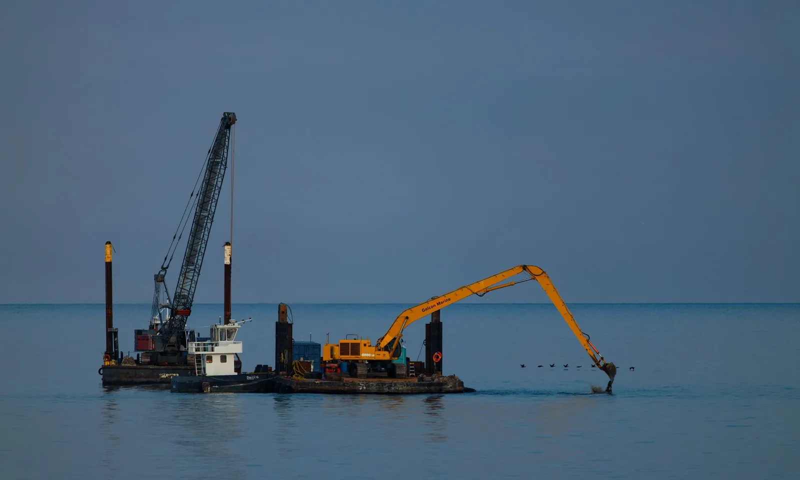 Dredging barge with crane operating at sea under clear sky. Stock photo illustrating Knowledge Marine & Engineering Works' earning call story.