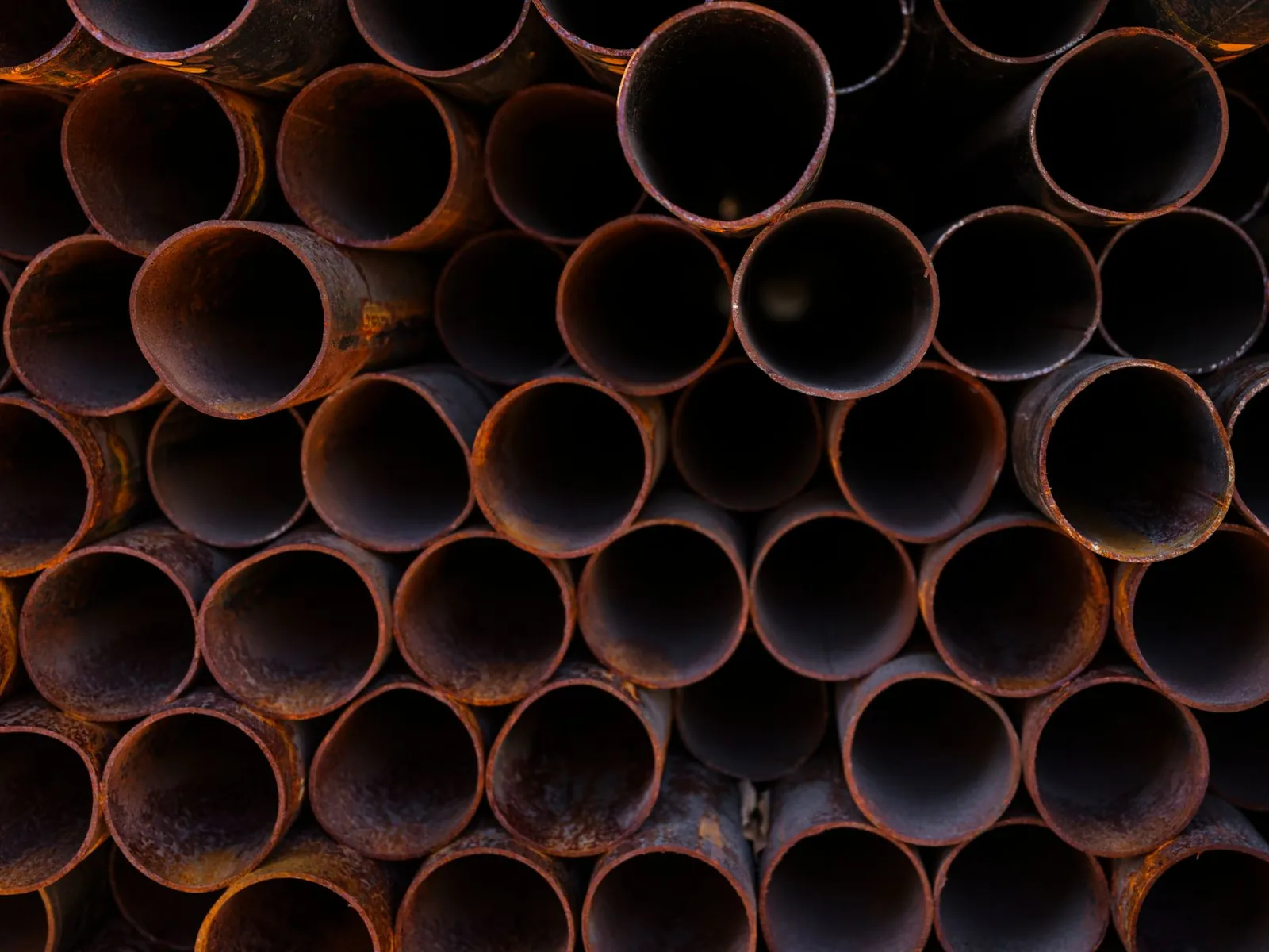 Close-up view of stacked rusty industrial pipes, showcasing their texture and corrosion. Stock photo illustrating Electrosteel Castings' promoter buying story.