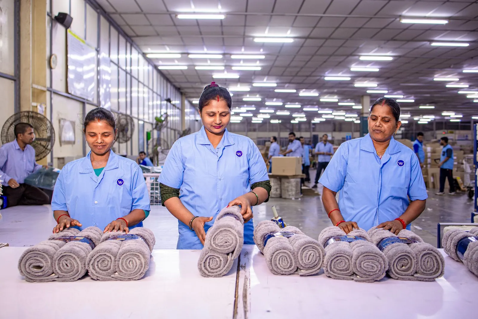 Three female workers inspecting rolled towels at a textile factory, showcasing teamwork and quality control. Stock photo illustrating Auro Laboratories' regulatory approval story.