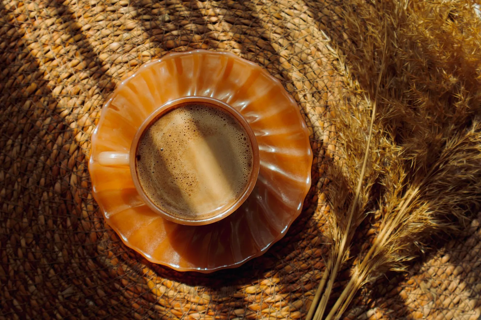 Coffee cup on woven mat with dried grass, warm natural light. Stock photo illustrating Vintage Coffee And Beverages' earning call story.