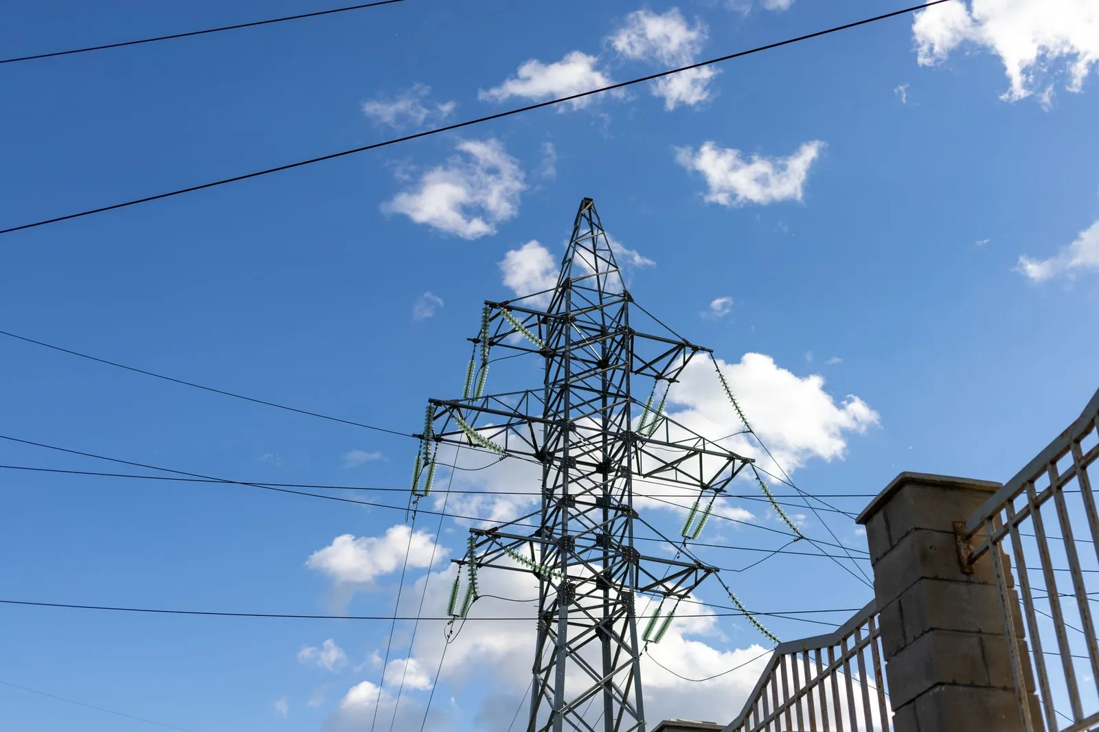 High voltage transmission tower against a clear blue sky with clouds. Stock photo illustrating Bajel Projects' new order story.
