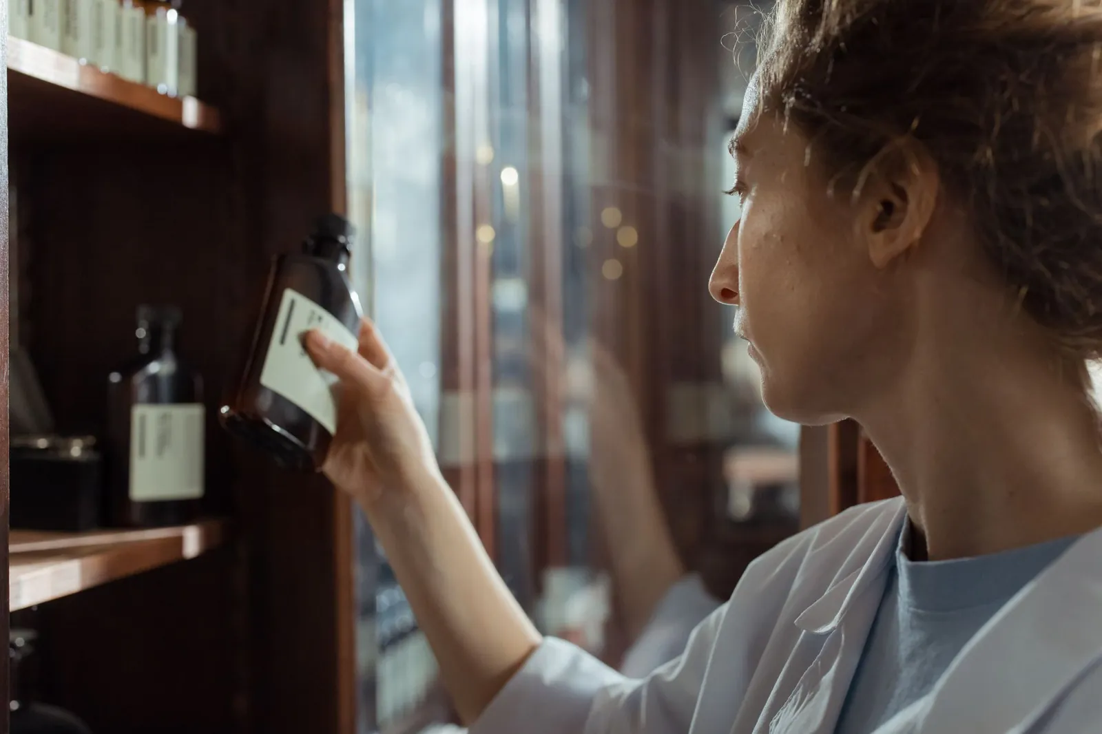 A pharmacist in a lab coat selecting a medication bottle from a pharmacy shelf indoors. Stock photo illustrating Lupin's earning call story.