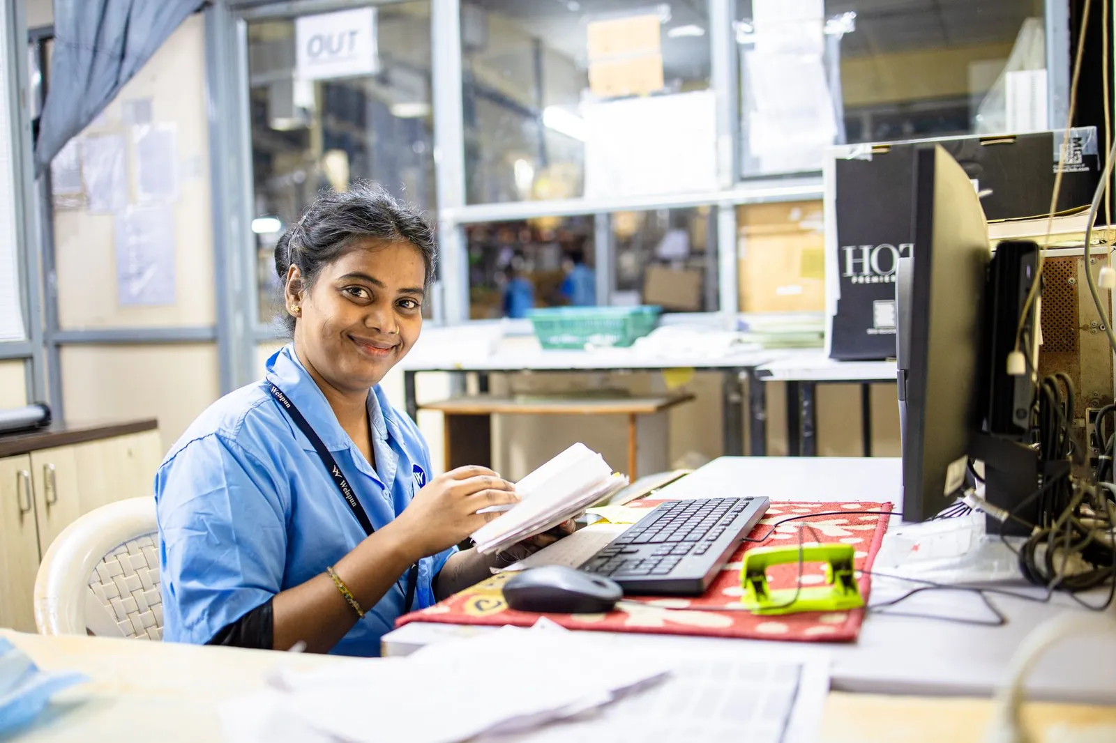 A cheerful female worker seated at her desk in an office setting, reviewing documents. Stock photo illustrating Spandana Sphoorty Financial's financial results story.