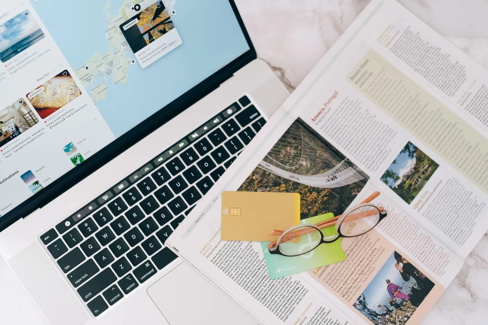 A top view of travel planning essentials on a laptop with a map, credit cards, and a magazine. Stock photo illustrating TBO Tek's earning call story.