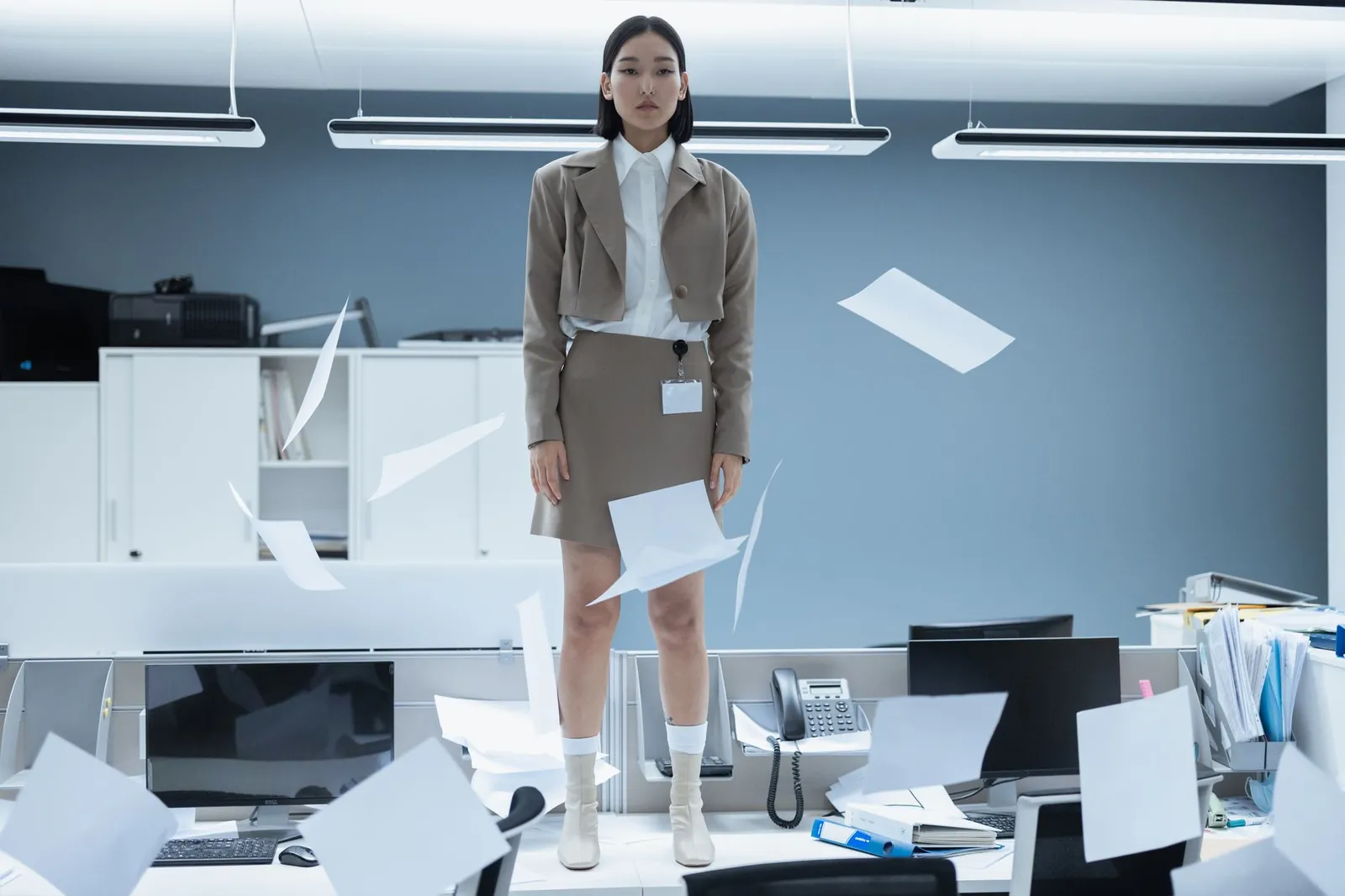 Fashionable young woman standing on a desk in a minimalist office with papers flying. Stock photo illustrating Active Clothing Co's expansion story.