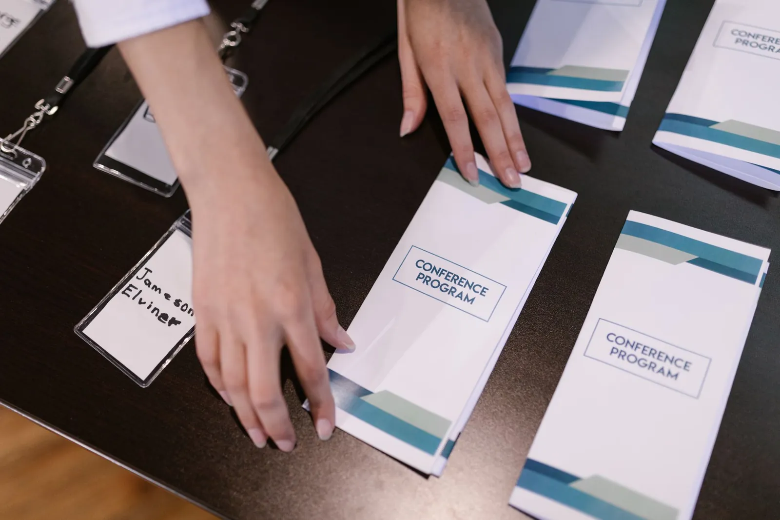 Hands organizing conference programs and name tags at event registration desk. Stock photo for the ALFA News guide: Material Event Disclosure in India: A SEBI Guide.