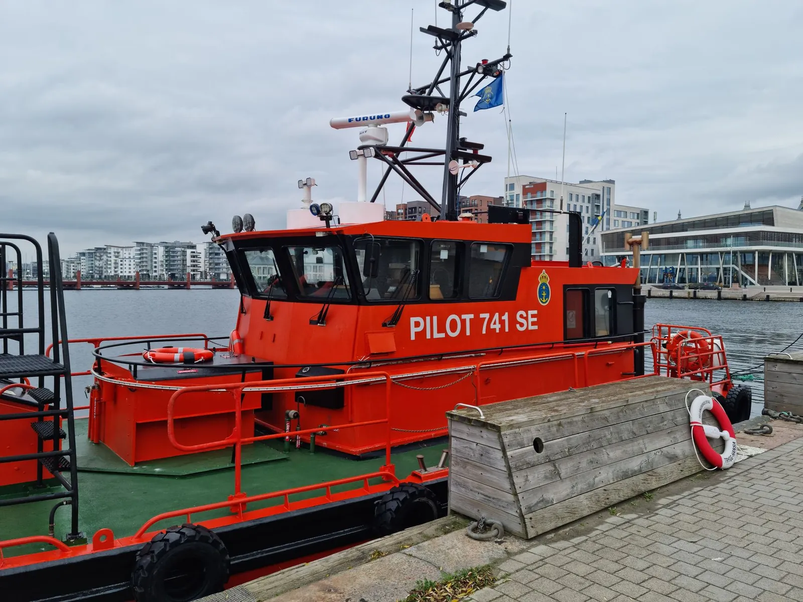 Vibrant red pilot boat docked in a harbor with urban backdrop. Stock photo illustrating Sadhav Shipping's new order story.