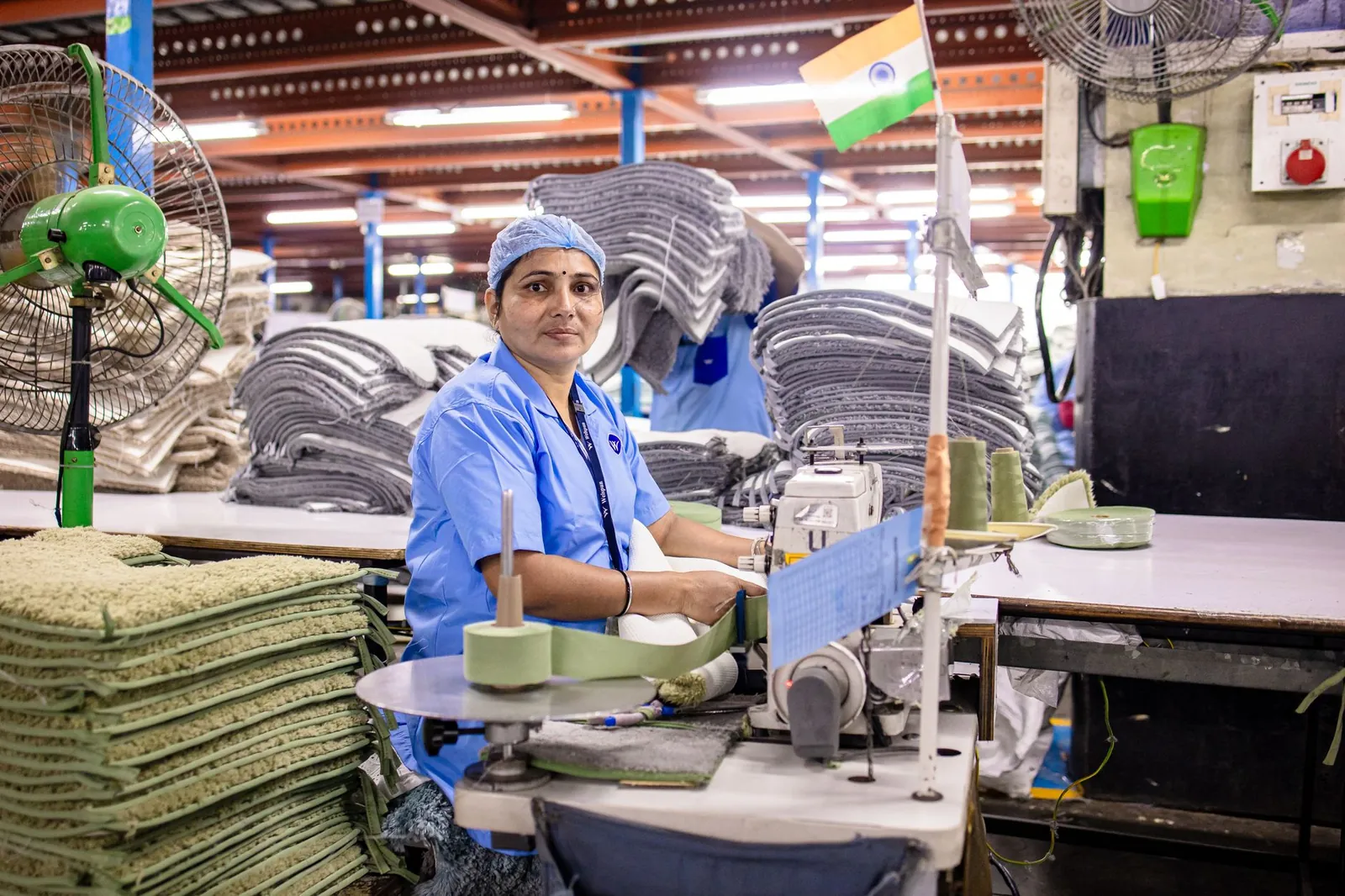 A female factory worker sewing textiles in an Indian factory, surrounded by fabrics. Stock photo illustrating Swaraj Suiting's fund raise story.