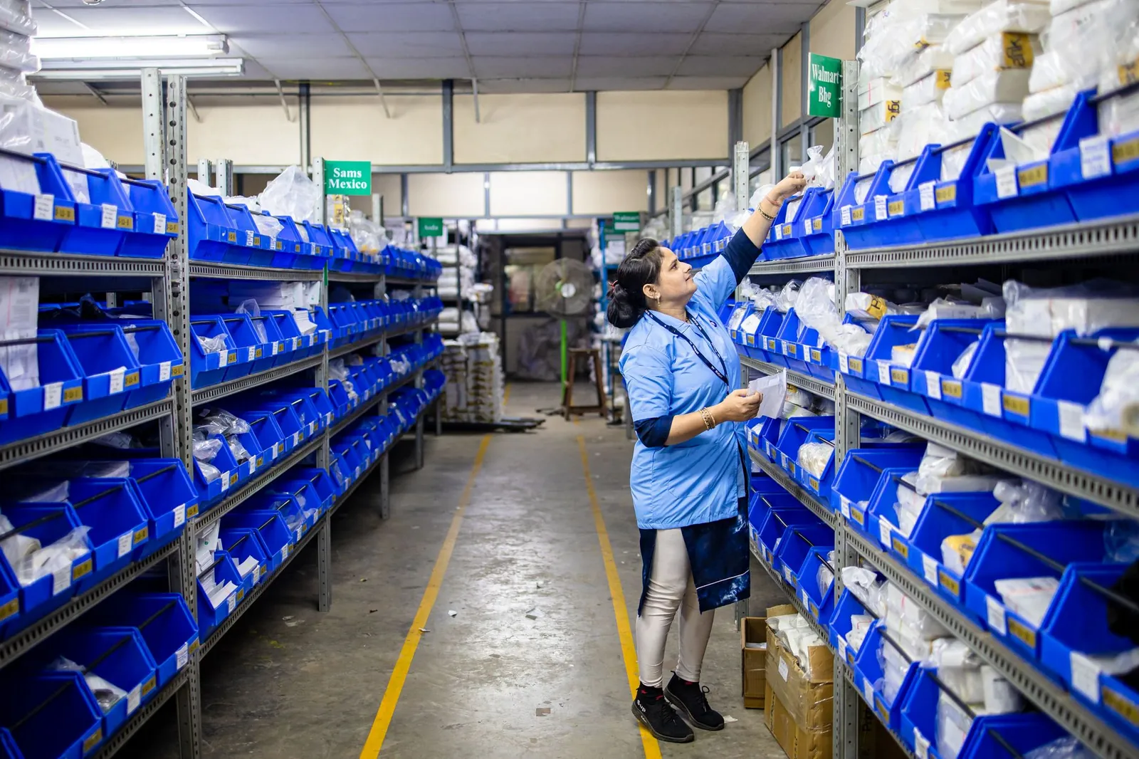 Woman in uniform organizing inventory in a warehouse aisle with labeled bins. Stock photo illustrating Unicommerce eSolutions' expansion story.