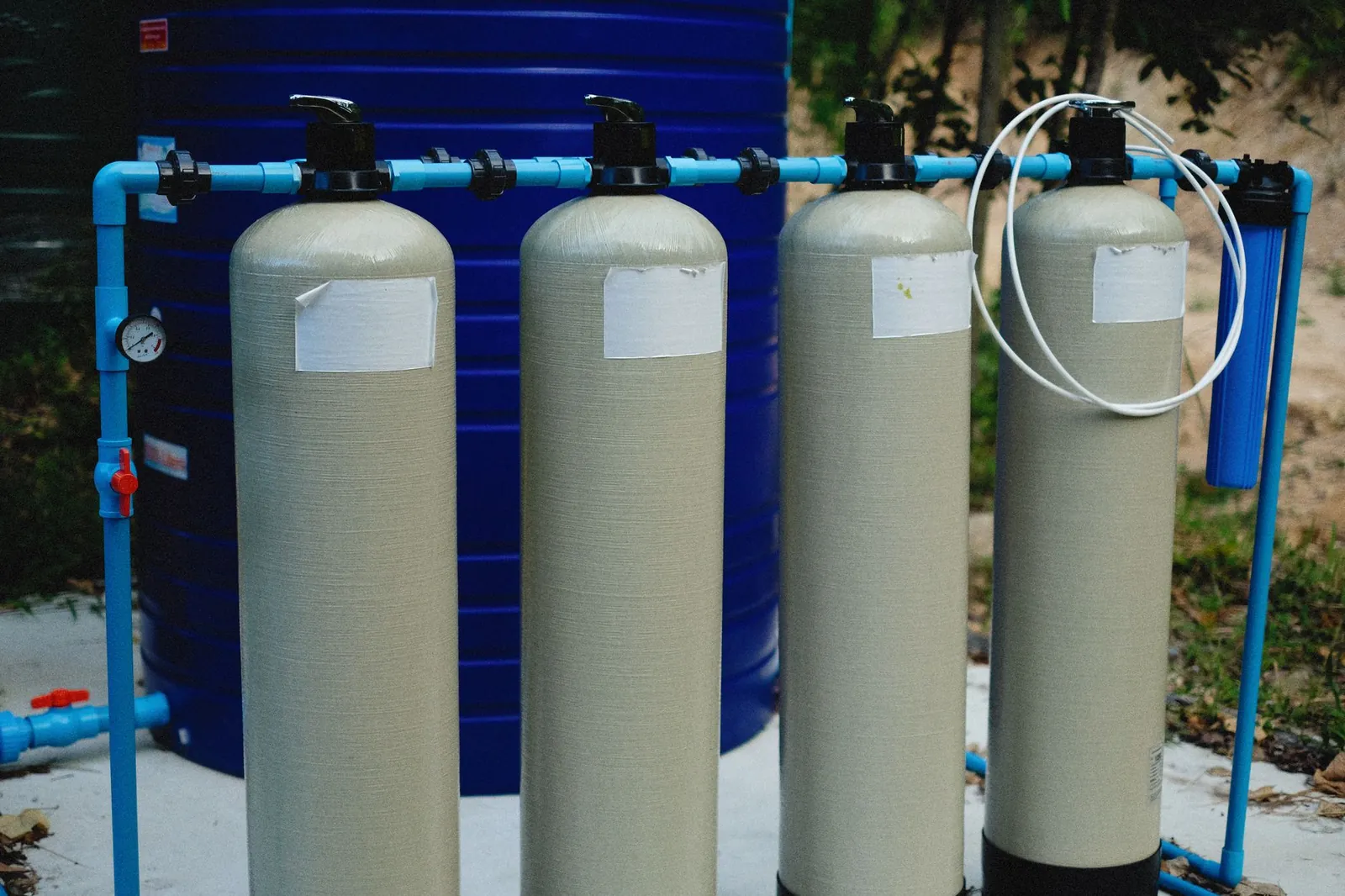 Four beige tanks in an outdoor water treatment setup with blue piping. Stock photo illustrating Felix Industries' earning call story.