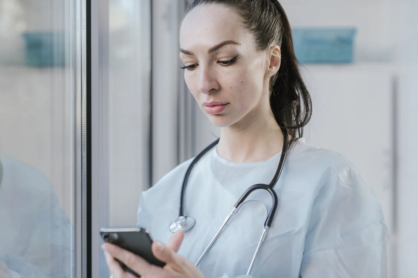 Portrait of a female doctor in a disposable gown using a smartphone in a hospital environment. Stock photo illustrating Emerald Finance's partnership story.