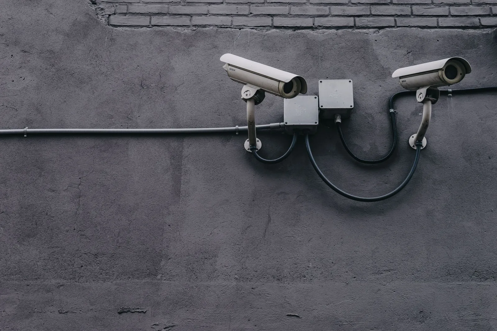 Two surveillance cameras mounted on a concrete wall, highlighting security technology. Stock photo illustrating Aditya Infotech's earning call story.