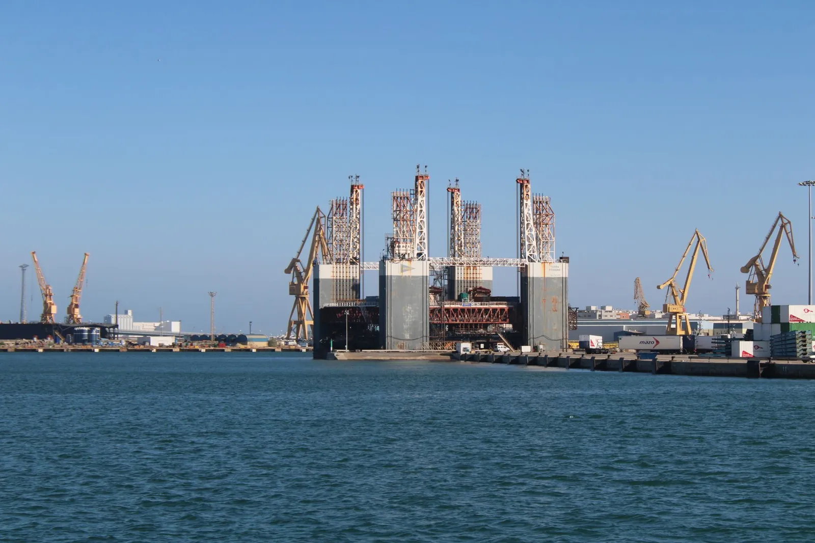 View of Cádiz industrial port with cranes and oil rig on a sunny day. Stock photo illustrating JSW Infrastructure's fund raise story.