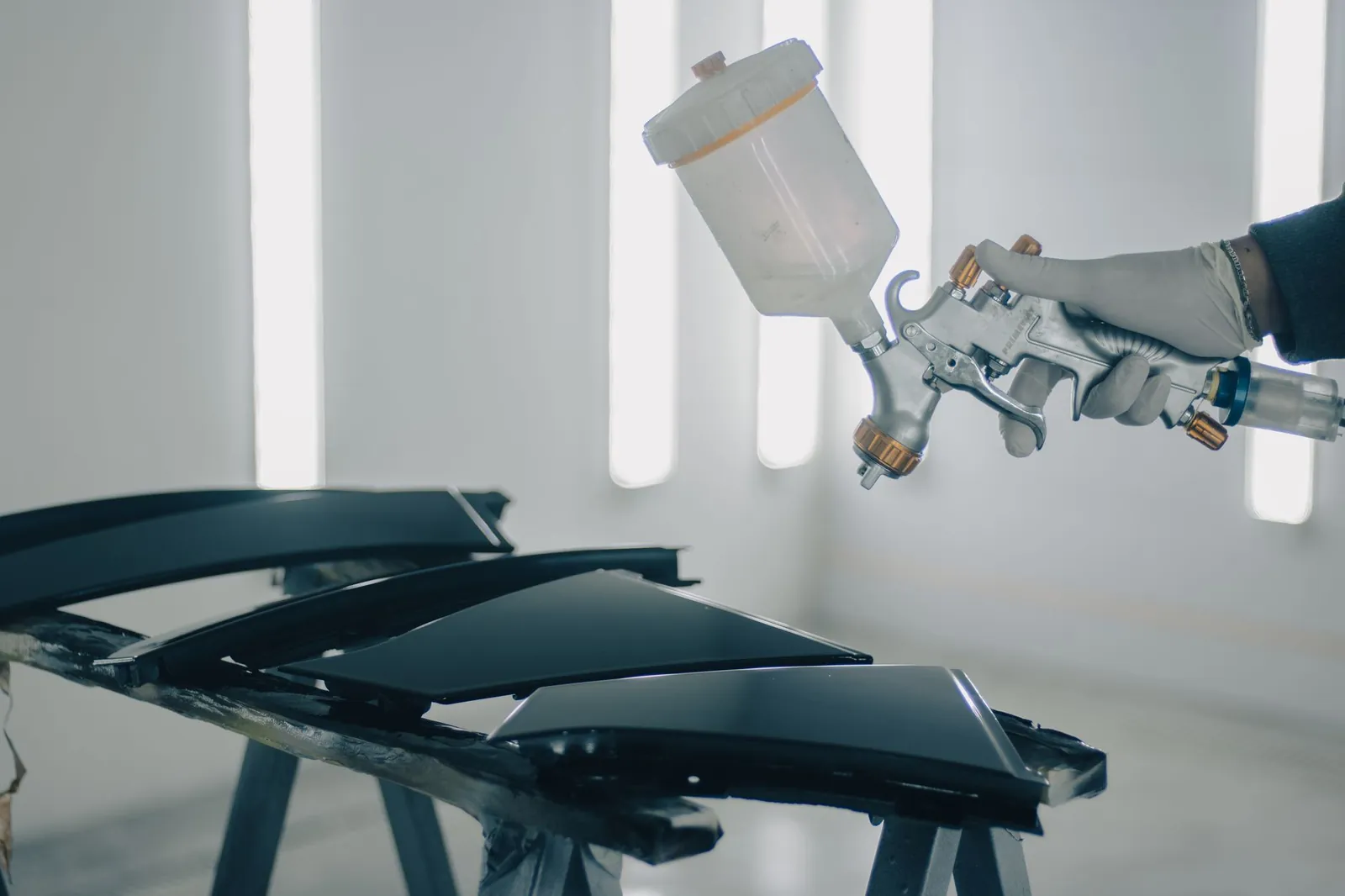 Close-up of car parts being spray-painted in an automotive workshop. Stock photo illustrating Garware Hi-Tech Films' partnership story.