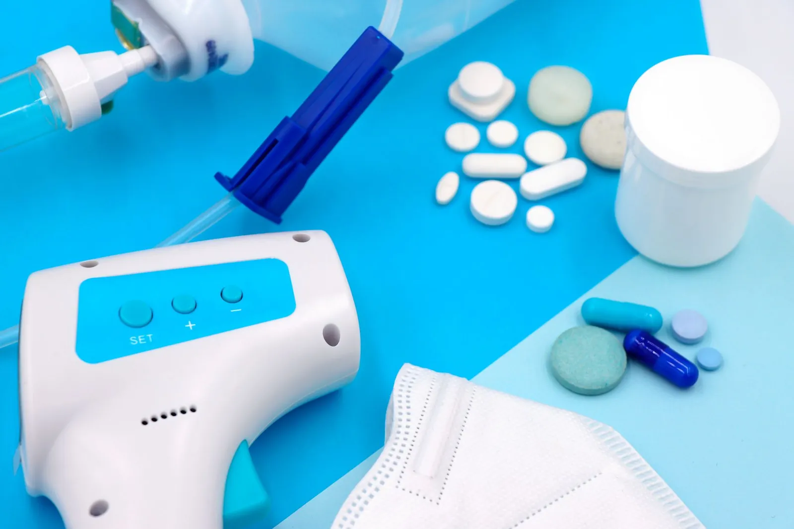 A collection of medical supplies including pills, a mask, and a thermometer on a blue surface. Stock photo illustrating Tata Elxsi's product launched story.