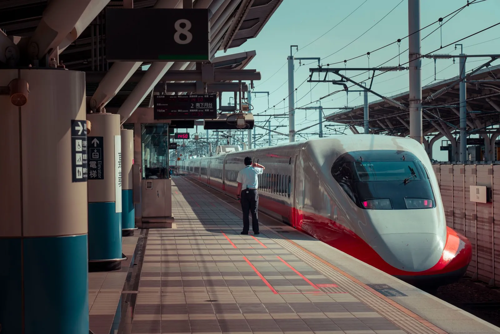 Back view of unrecognizable male worker standing on platform of railway station near modern high speed train on sunny day. Stock photo illustrating BEML's new order story.