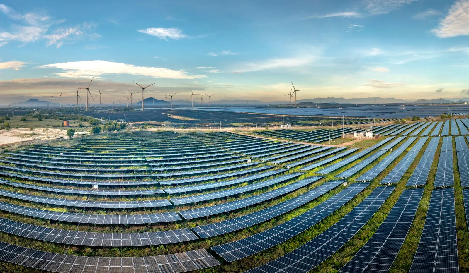 Expansive solar farm with wind turbines in the background under a clear blue sky. Stock photo illustrating Waaree Renewable Technologies' new order story.