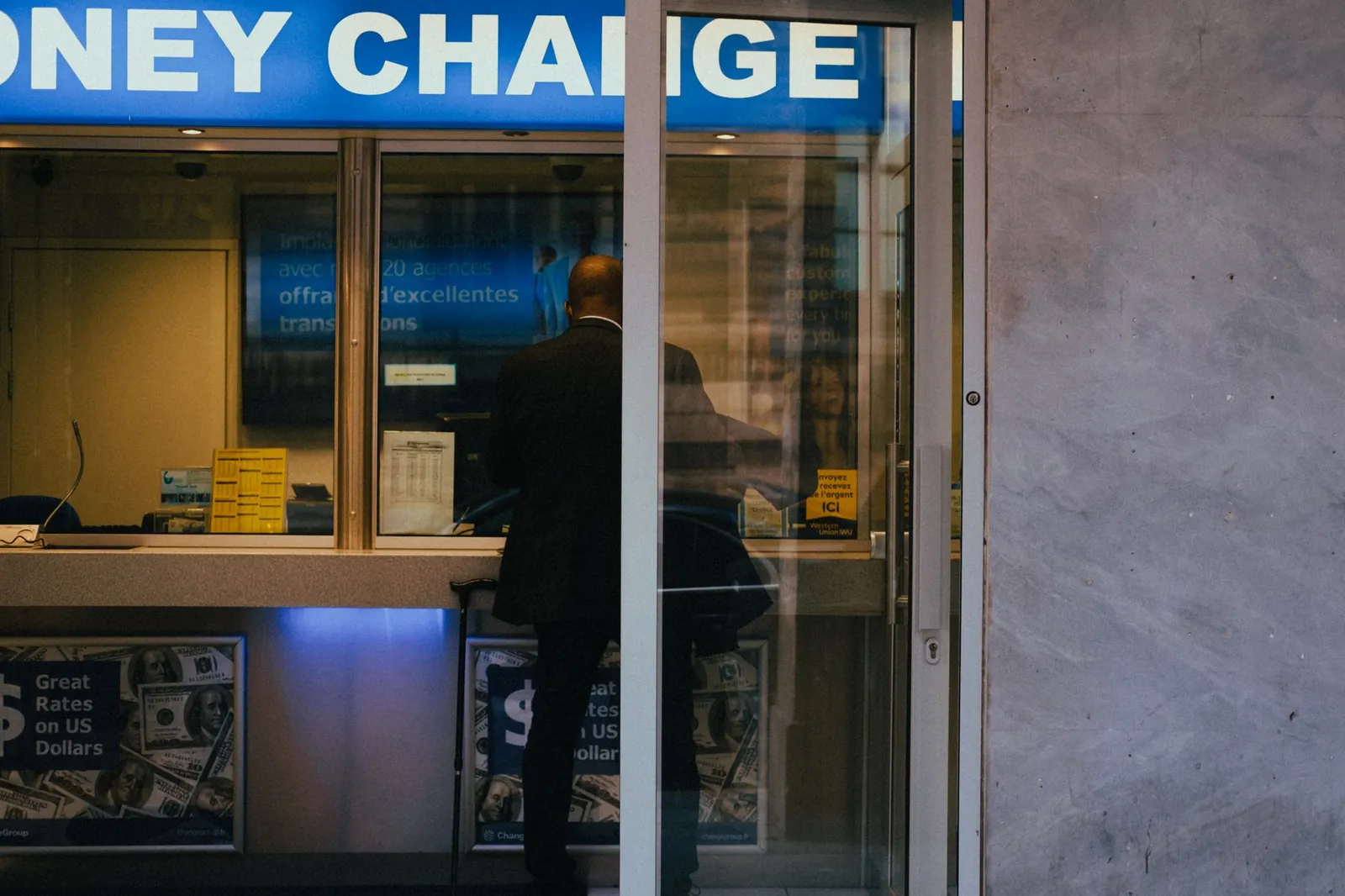 Man at a currency exchange office window, showing currency rates inside a bustling city. Stock photo for the ALFA News guide: Clarification Sought by the Exchange: What It Means for a Stock.