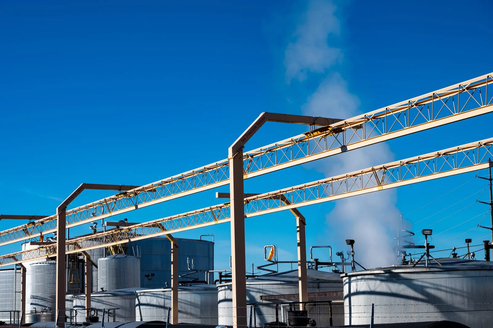 Wide view of an industrial plant with smoke rising from storage tanks against a clear blue sky. Stock photo illustrating Aarti Industries' fund raise story.