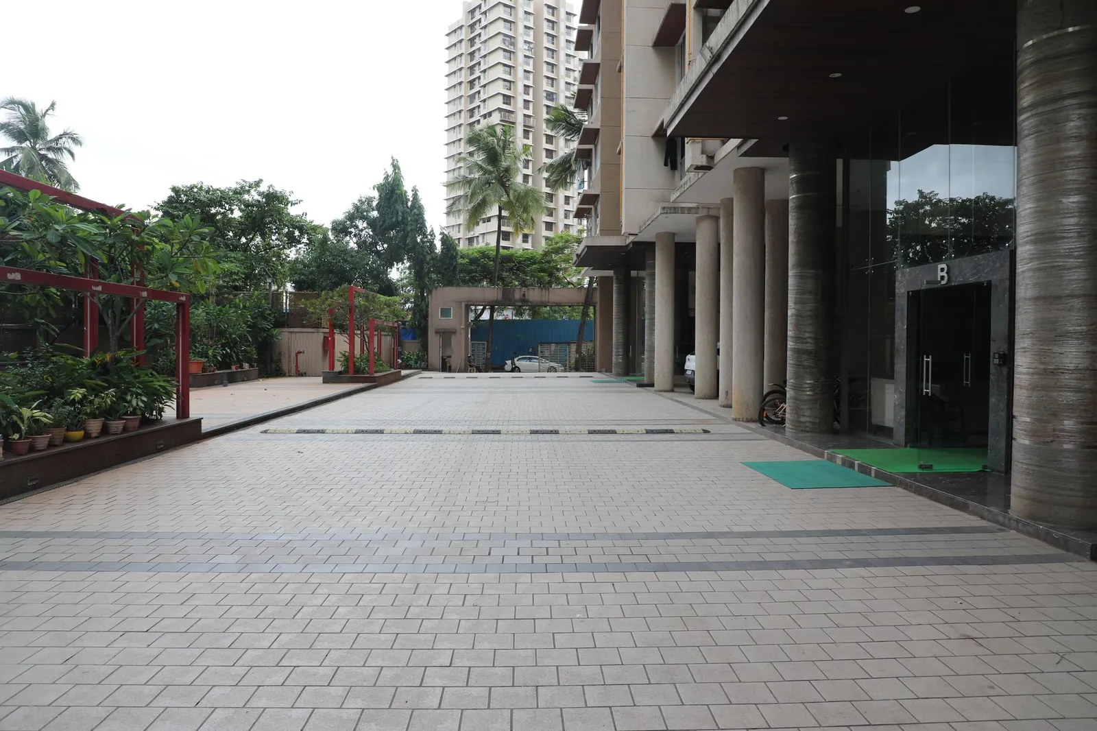 Spacious apartment complex exterior featuring tiled walkway, greenery, and tall residential building. Stock photo illustrating Arisinfra Solutions' new order story.