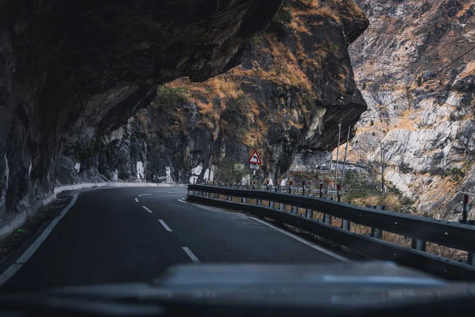 Curved road through a dramatic Himalayan mountain pass under rocky overhang. Stock photo illustrating SRM Contractors' earning call story.