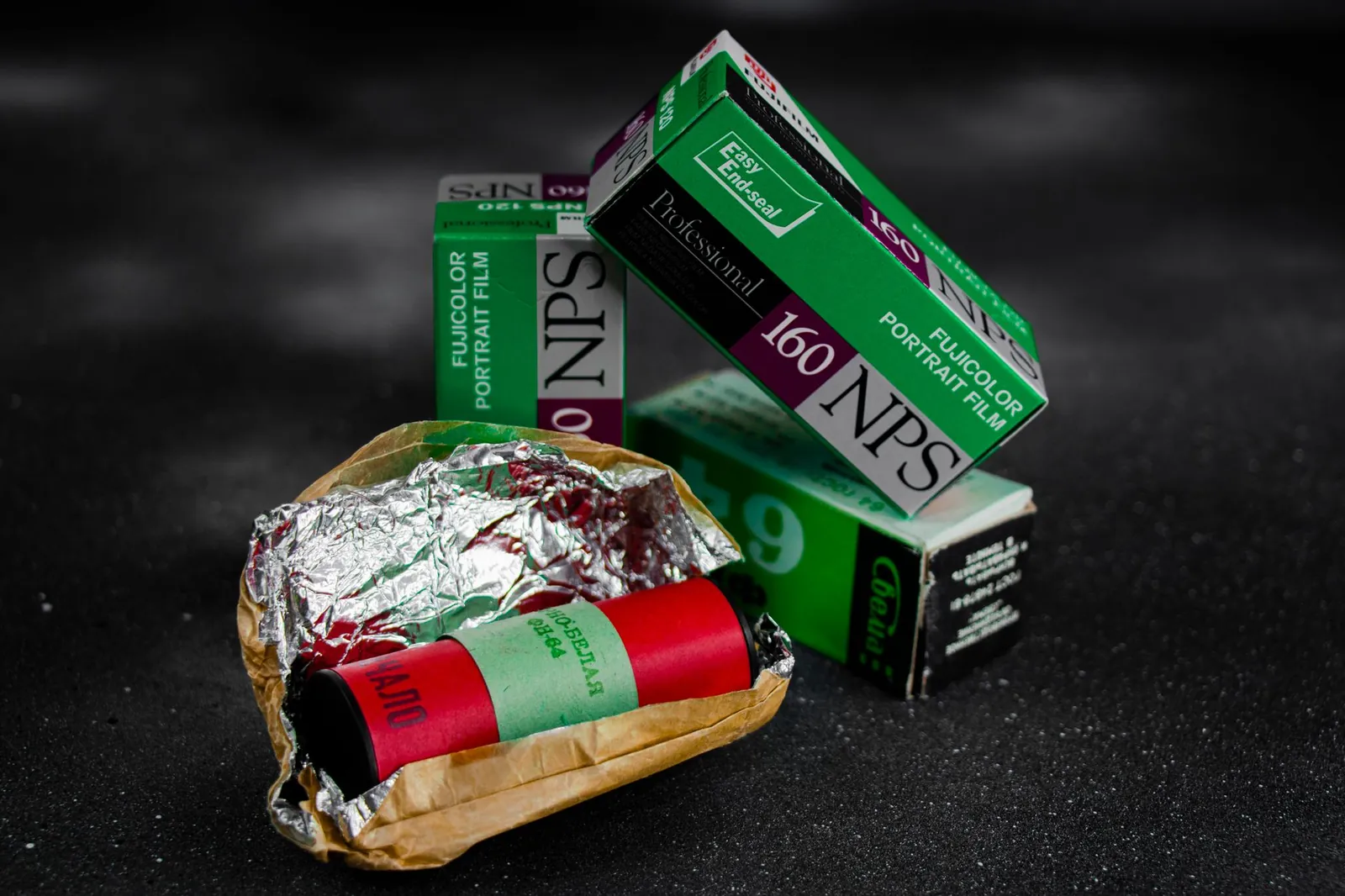 Vintage Fujicolor portrait film rolls and packaging on a textured black surface. Stock photo illustrating Cosmo First's earning call story.