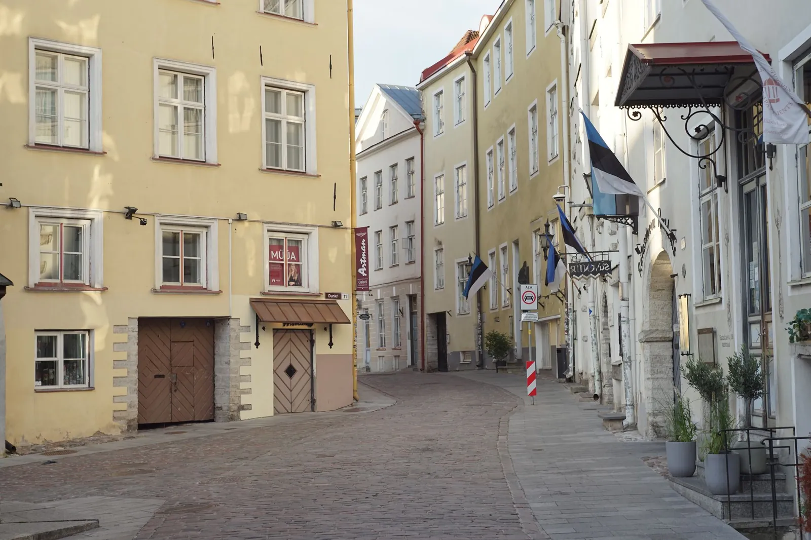 A picturesque cobblestone street in Tallinn's Old Town, featuring historical buildings and Estonian flags. Stock photo illustrating Persistent Systems' expansion story.