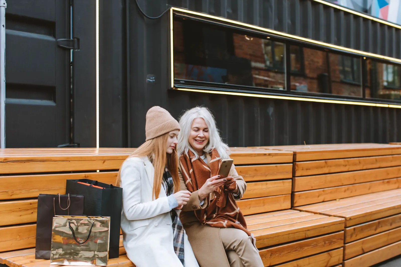 Elderly woman with teenage girl enjoying shopping day outdoors, bonding over smartphone. Stock photo illustrating D.P. Abhushan's product launched story.