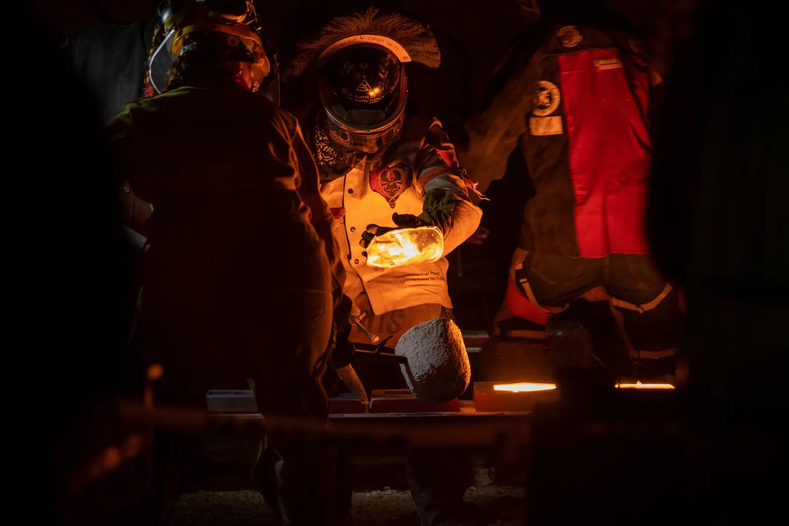 Workers in protective gear pour molten metal in a dark industrial setting. Dramatic lighting. Stock photo illustrating PTC Industries' fund raise story.