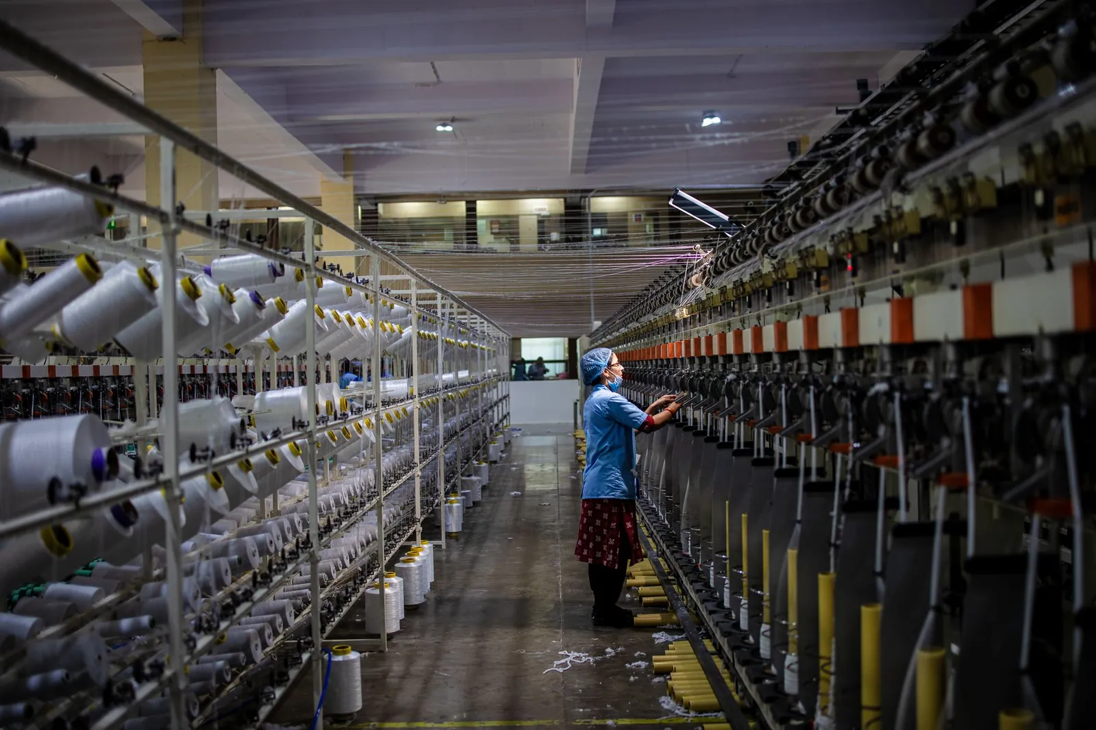 Textile factory worker monitoring machinery. Industrial and manufacturing setting. Stock photo illustrating Natco Pharma's fund raise story.