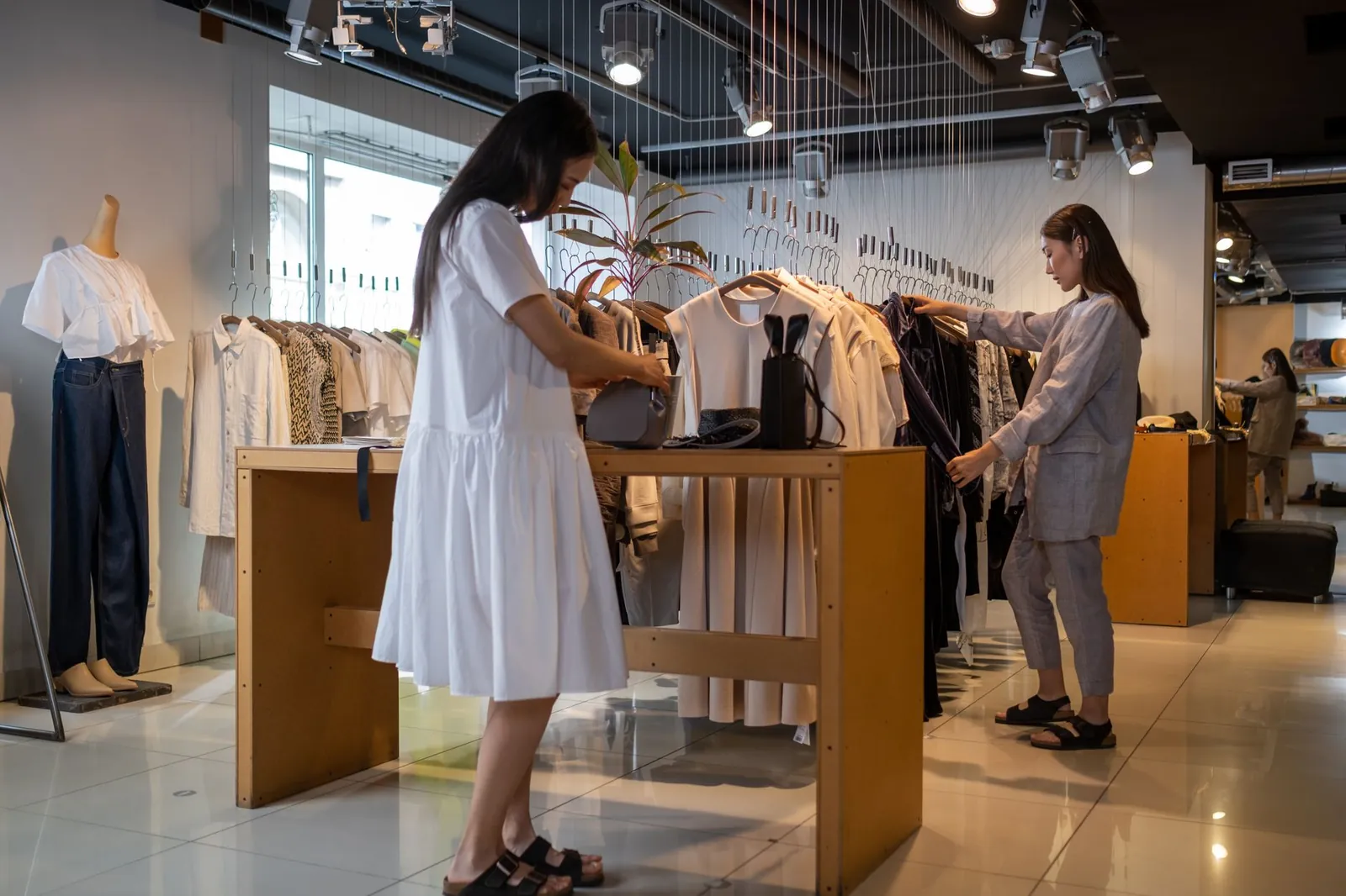 Two women browsing clothes in a modern indoor fashion store. Stock photo illustrating Thomas Scott (India)'s partnership story.