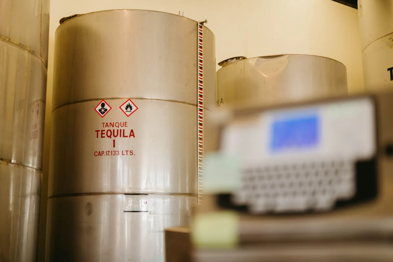 Close-up of tequila storage tanks in a distillery with safety warnings, showcasing tequila production. Stock photo illustrating Modi Naturals' earning call story.