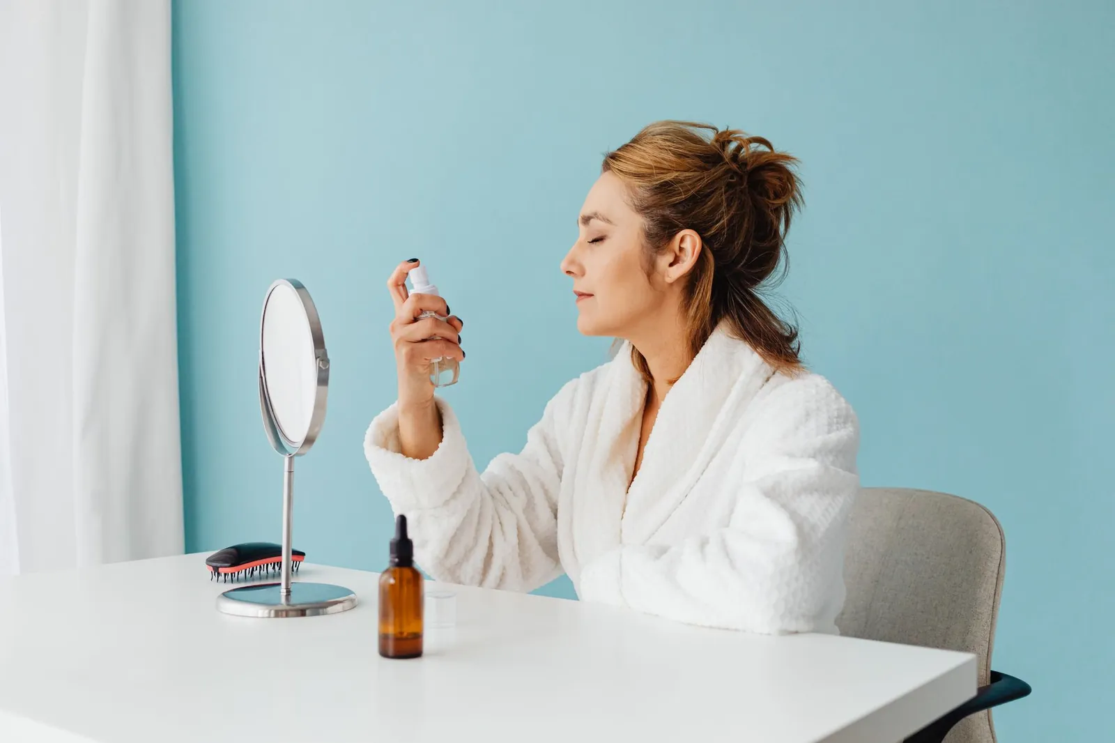 Woman in bathrobe using a spray bottle for skincare during a self-care routine indoors. Stock photo illustrating Glenmark Pharmaceuticals' product launched story.