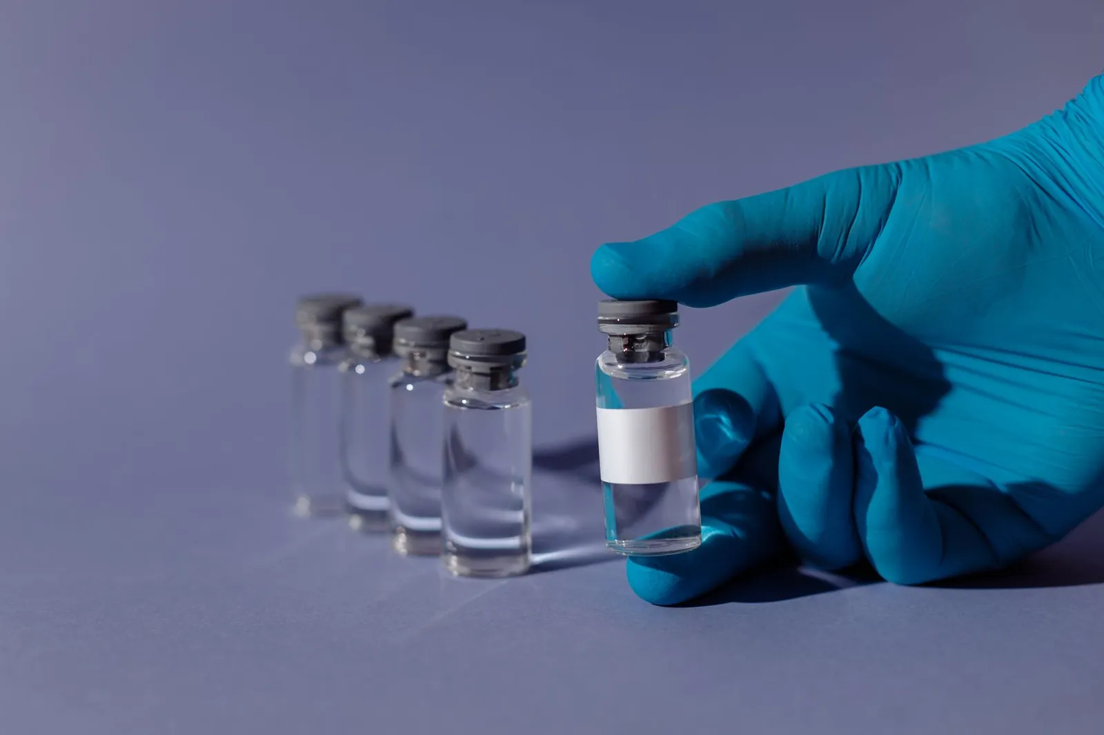Blue-gloved hand holding a transparent vial with liquid, representing healthcare and vaccination. Stock photo illustrating Glenmark Pharmaceuticals' product launched story.